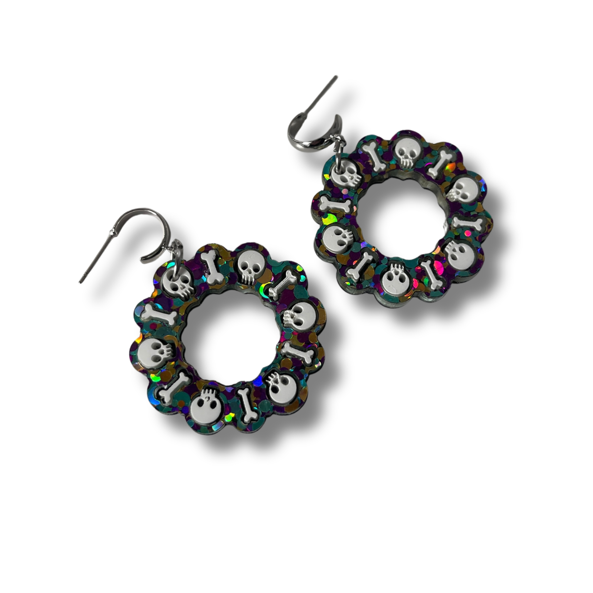 Pendientes de metacrilato glitter multicolor con diseño circular de calaveras y huesos sobre fondo blanco con el logo de Minipekas.